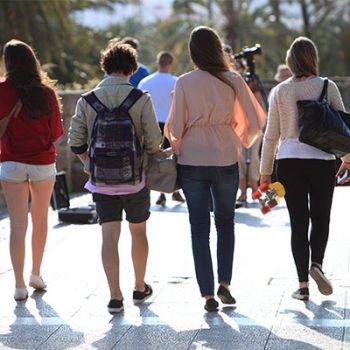 Backs of four teenagers walking away from camera in a line.